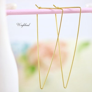 May include: A pair of gold triangle shaped earrings hanging from a pink stand.