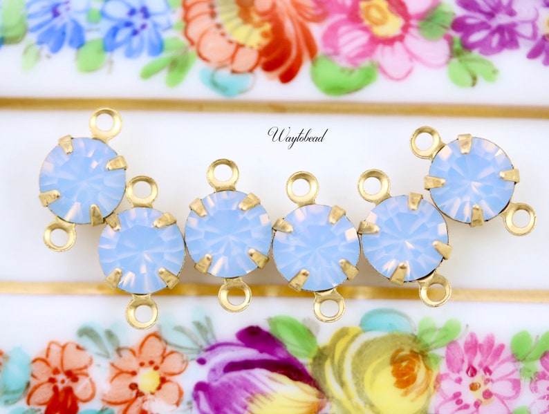 Puede incluir: Cinco conectores de charms de tono dorado con piedras de color azul claro que parecen &oacute;palo. Cada charm tiene dos anillos de salto.