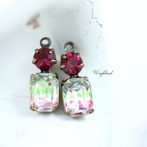 May include: Two-piece earring charms featuring a red crystal and a clear iridescent crystal. The charms are attached to a brass loop.