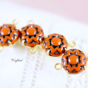 May include: Four orange and black patterned round beads with gold metal loops. The beads have a starburst design.
