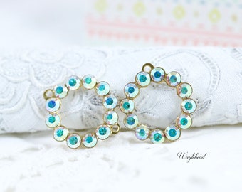 Puede incluir: Dos anillos de metal dorado con un círculo de piedras de cristal azules iridiscentes alrededor del perímetro. Los anillos están sobre un fondo de encaje blanco.