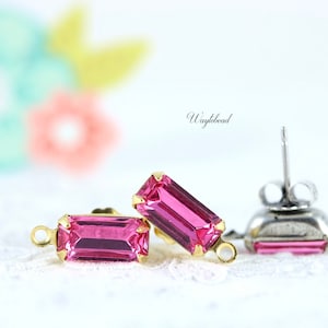 May include: A pair of pink rectangular earrings with gold settings and a silver post. The earrings are on a white lace background.