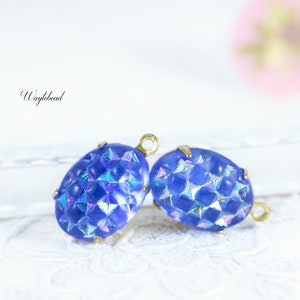 May include: Two blue glass oval-shaped beads with a textured surface and gold metal loops. The beads have an iridescent finish.
