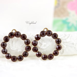 May include: Two antique gold-toned metal charms with a circle design. Each charm is adorned with a ring of dark red rhinestones.