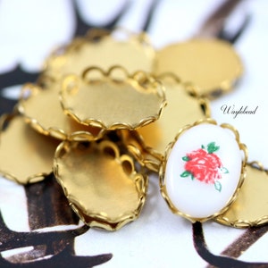 May include: A group of gold-coloured metal oval-shaped pendant trays with a scalloped edge. One tray has a white cameo with a red rose design.