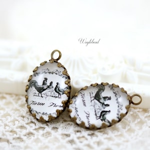 May include: Two oval-shaped glass charms with a bronze-colored metal frame. The charms feature a black and white image of roosters and the text "Farm Fresh".