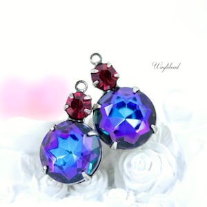 Puede incluir: Un par de pendientes con una piedra preciosa azul y púrpura iridiscente y una piedra preciosa roja. Los pendientes están sobre un fondo blanco.