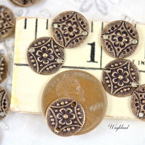 May include: A close-up of antique brass-toned metal buttons with a floral design. The buttons are arranged on a wooden surface with a ruler and a US penny for scale.