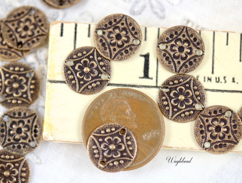 May include: A close-up of antique brass-toned metal buttons with a floral design. The buttons are arranged on a wooden surface with a ruler and a US penny for scale.