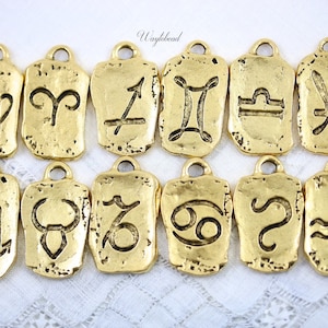 May include: Twelve gold-toned metal charms featuring the astrological signs of the zodiac. Each charm is shaped like a rough stone with a raised design of the zodiac symbol.