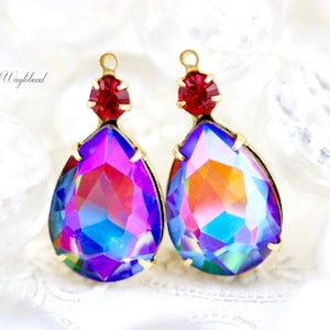 May include: Two teardrop-shaped pendants with a vibrant, iridescent finish. Each pendant features a large, faceted crystal in shades of purple, blue, and orange, set in a gold-tone metal frame. A small, red crystal tops each pendant. The text "Wayfobead" is in the image.