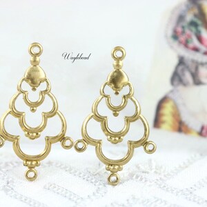 May include: Two gold-tone metal earring findings with a decorative, openwork design resembling a stylized tree or chandelier. Each finding has three loops for attaching jewelry components.