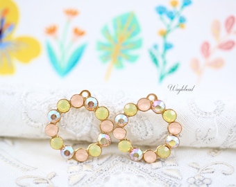 Puede incluir: Dos anillos de metal dorado con un círculo de piedras de imitación de color rosa pastel, amarillo e iridiscente.