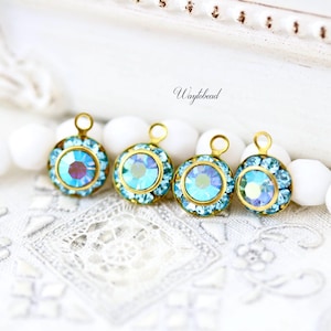 May include: Four round, gold-toned pendants with iridescent blue and purple crystals. Each pendant has a smaller, central crystal surrounded by a ring of smaller blue crystals. The pendants are displayed on a white, textured surface.
