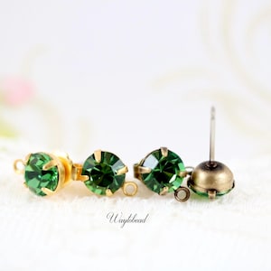 May include: Close-up of three green gemstone stud earrings with gold-colored settings. One earring has a post, while the others have loops. The earrings are displayed on a white, textured surface.
