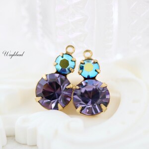 May include: A pair of earrings with a gold-tone setting and three round, faceted gemstones. The top gemstone is a light blue color, and the bottom two gemstones are a deep purple color.