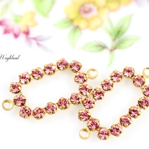 May include: Two gold-toned metal oval-shaped frames with pink rhinestones. Each frame has a loop on either side.