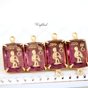 May include: Four gold-tone charms with pink glass insets featuring the astrological sign Aquarius. Each charm has a loop at the top for attaching to a necklace or bracelet.