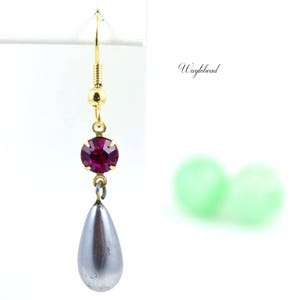 Puede incluir: Un par de pendientes colgantes con una perla en forma de l&aacute;grima y un peque&ntilde;o strass redondo de color morado oscuro.