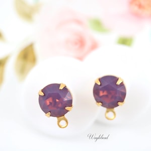 May include: Two gold-toned earring findings with a purple glass stone in the center. The stones have a faceted design.