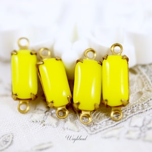 May include: Four yellow glass rectangular beads with gold metal settings and jump rings. The beads are on a white lace background.