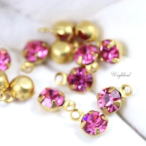 May include: A close-up of pink rhinestone charms with gold-toned settings and jump rings. The charms are scattered on a white surface. The text "Waybead" is visible in the lower right corner of the image.