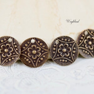 May include: Four antique brass-colored metal charms with a floral design and a hole for hanging. The charms are round and have a textured surface.