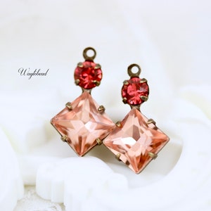 Puede incluir: Un par de pendientes con un cristal rosa de forma cuadrada y un cristal rojo más pequeño en la parte superior. Los pendientes están hechos de latón y tienen un aspecto vintage.