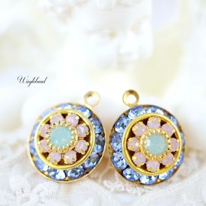 May include: A pair of gold-toned earrings with a blue and pink flower design. The earrings have a round shape and are decorated with small blue and pink crystals.
