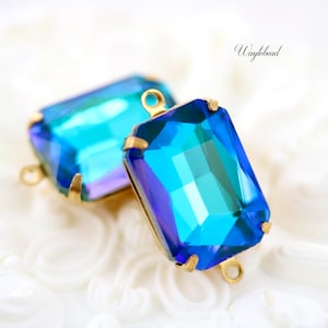 May include: Two blue glass rectangular pendant charms with gold metal loops. The charms have a faceted design and a blue to teal color gradient.