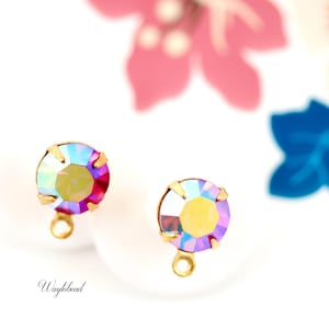 May include: Two iridescent purple and pink glass beads with gold settings and loops. The beads are on a white surface.