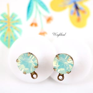 May include: Two light blue opal gemstone earring findings with silver-toned metal loops. The findings are on a white surface with a floral pattern.