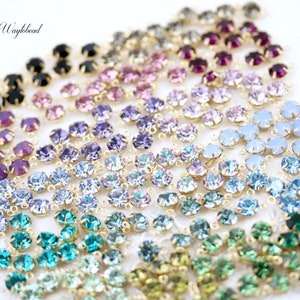Puede incluir: Surtido de cuentas de cristal de colores con anillos de salto dorados. Las cuentas est&aacute;n dispuestas en filas, cada fila con un color diferente. Los colores incluyen negro, morado, rosa, azul claro, azul, verde y turquesa.