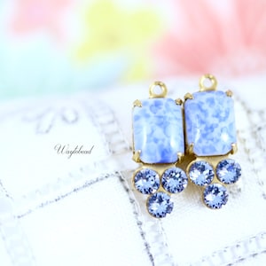 Puede incluir: Un par de pendientes azules y dorados con un encanto de vidrio azul de forma cuadrada y un grupo de diamantes de imitación azules.