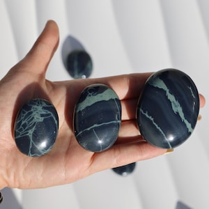 May include: Three smooth, polished stones with a dark blue and green marbled pattern. The stones are oval shaped and have a glossy finish.