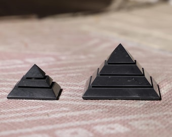 May include: Two black pyramid-shaped incense holders, one larger than the other, with multiple tiers. The holders are made of a smooth, black material and have a sleek, modern design.