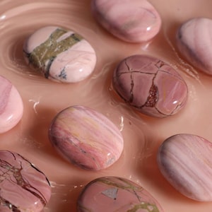 May include: A collection of polished stones in shades of pink and white, featuring a variety of patterns. The stones are smooth and have a glossy finish.