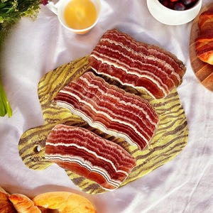 May include: Four slices of pink and white layered agate on a yellow and brown patterned wooden serving board.