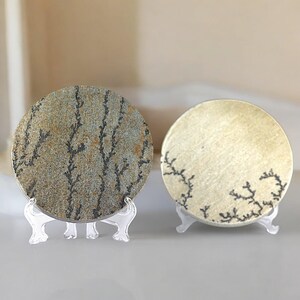 May include: Two round, decorative coasters with a dendritic pattern. The coaster on the left is gray with black dendrites, while the coaster on the right is beige with black dendrites.