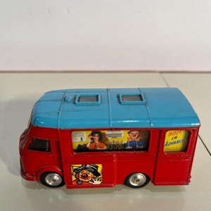 May include: A vintage toy bus in red and blue. The bus has small windows with images inside and the text "BOOK IN ADVANCE". A clown graphic is on the side.
