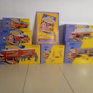 May include: A collection of Corgi Classics Chipperfield Circus toy trucks and trailers in their original boxes. The boxes are yellow and blue, featuring illustrations of circus performers, animals, and trucks. The text "Chipperfield Circus" is visible.