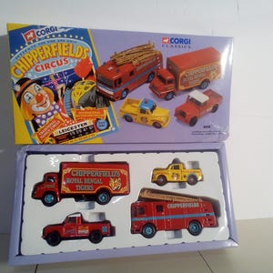 May include: A Corgi Classics Chipperfields Circus toy set. The set includes a box with a clown illustration and several miniature red, yellow, and orange trucks and vehicles. The box reads "Chipperfields Circus" and "Royal Bengal Tigers."