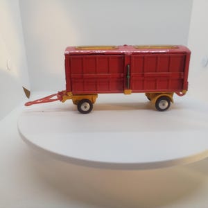 May include: A red toy wagon with yellow accents. The wagon has a rectangular body with two doors and a hitch. The wheels and undercarriage are yellow. The wagon is a vintage toy.