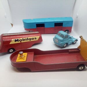 May include: A collection of vintage toy vehicles, including a red Mobilgas tanker truck, a blue and red bus, a blue truck, and a red flatbed truck with a yellow platform. These classic toys are likely from the mid-20th century.