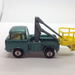May include: A vintage teal toy truck with a yellow lift bucket. The truck has black wheels and a gray lift arm. The toy truck is a miniature replica of a utility vehicle.