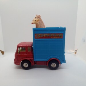 May include: A red and blue toy truck with the words "CHIPPERFIELDS CIRCUS" on the side. Two giraffe figurines are visible in the truck's cargo area. The toy truck has black wheels.