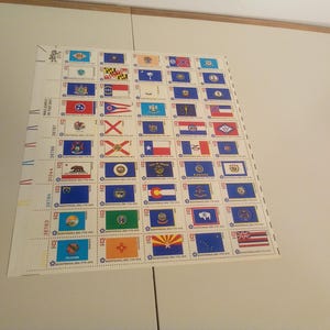 May include: A sheet of 50 US state flag stamps. Each stamp features a different state flag with the state name and year of statehood printed below. The stamps are arranged in rows and columns on a white background.