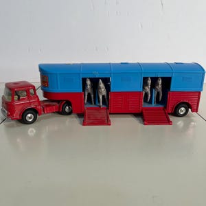 May include: A vintage toy circus truck in red and blue, with the words "Big Circus" on the side. The truck has a trailer with four horse figures inside, and red ramps extend from the trailer.