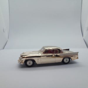 May include: A silver toy car model of a classic coupe with red interior. The car has a chrome bumper and a detailed exterior.