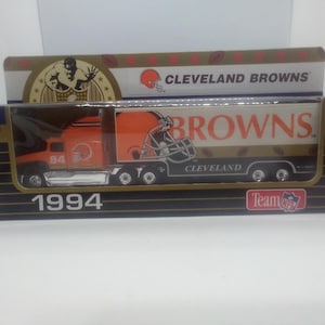 May include: A 1994 Cleveland Browns semi-truck toy in its original packaging. The orange truck features the team logo and number 94. The trailer is white with the word BROWNS and a helmet graphic. The box displays the NFL Team logo.